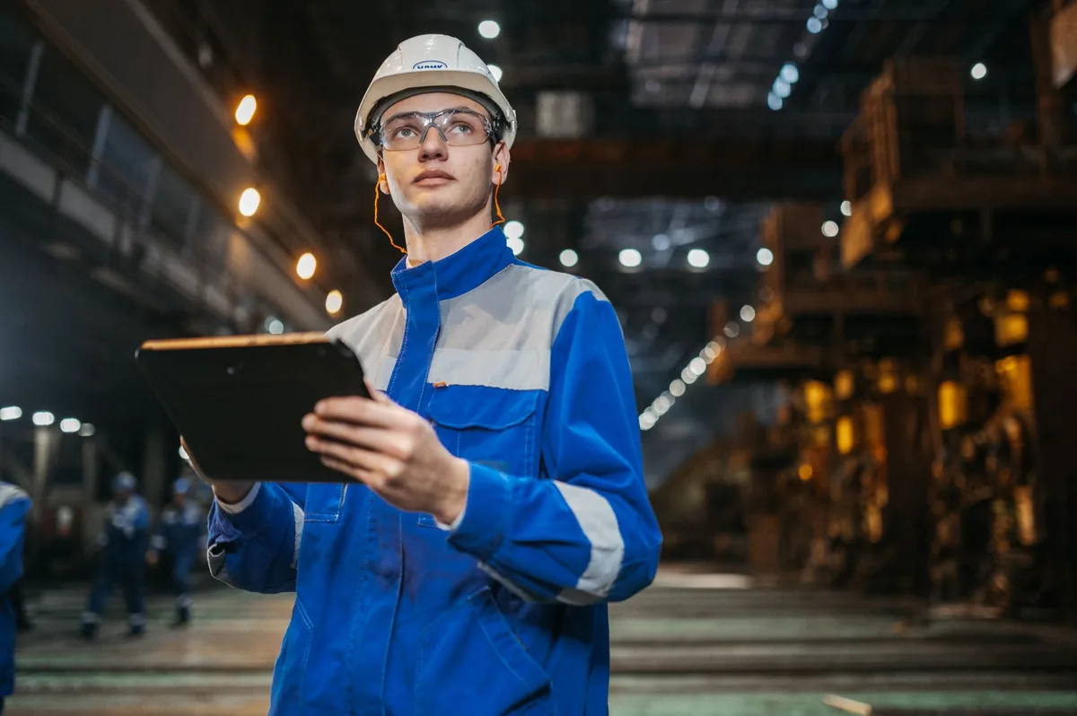 Engineer in safety gear reviewing industrial equipment with a tablet